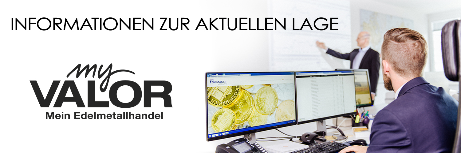 Ein Mann mit Anzug sitzt vor zwei Monitoren in einem modernen Büro. Die Bildschirme zeigen Finanzdaten und Bilder von Goldmünzen. Im Hintergrund präsentiert ein weiterer Mann in Anzug Informationen an einem Whiteboard. Links im Bild steht der Schriftzug 'Informationen zur aktuellen Lage' sowie das Logo von 'myVALOR – Mein Edelmetallhandel'.